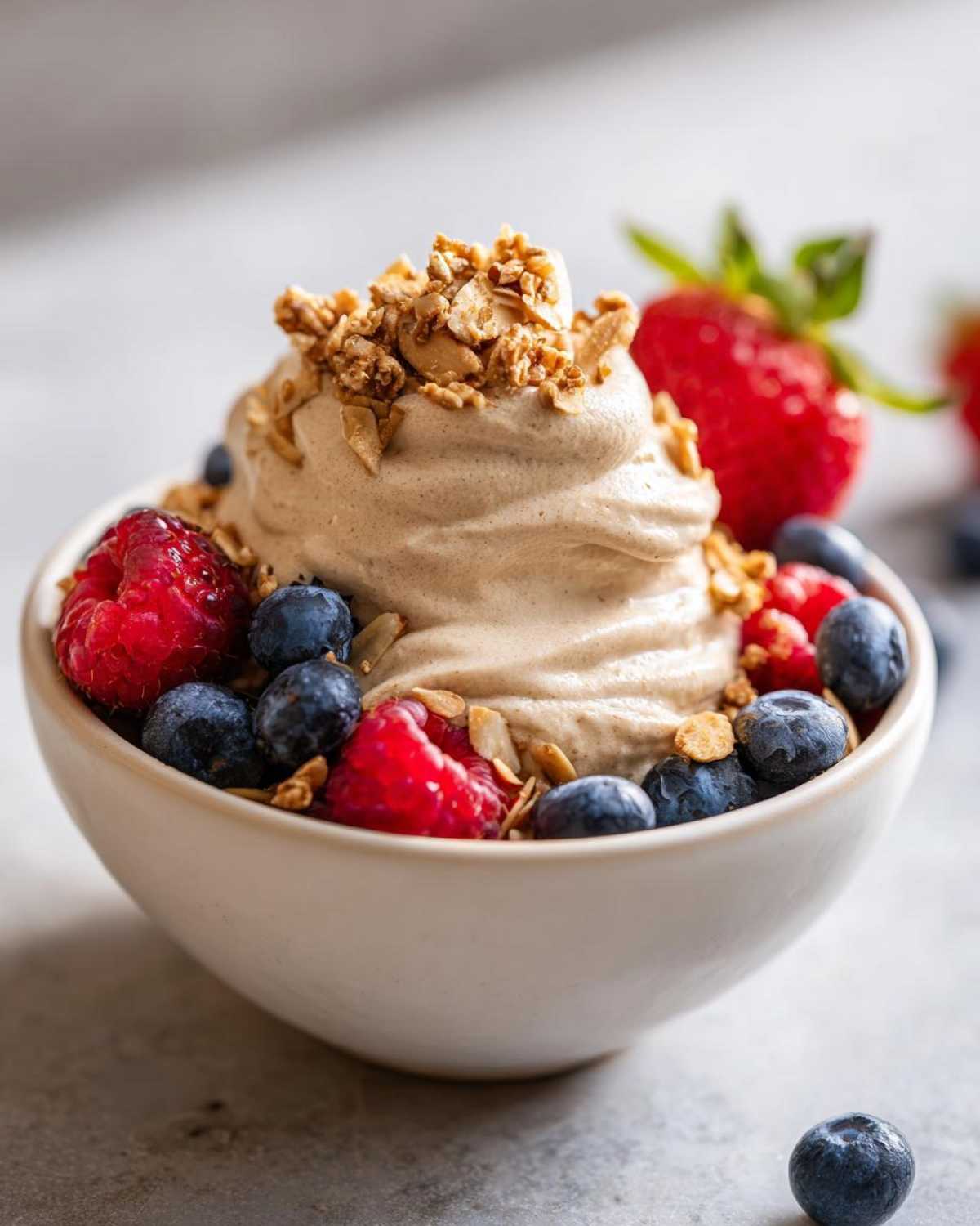 A swirl of Creamy Vanilla Protein Smoothie Bowl topped with granola, raspberries, and blueberries.