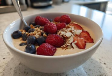 A close-up of a Creamy Vanilla Protein Smoothie Bowl topped with fresh raspberries, blueberries, sliced strawberries, and almonds.