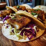 Close-up of three Crispy Baked Fish Tacos filled with crunchy red and green slaw and topped with seasoned white fish.