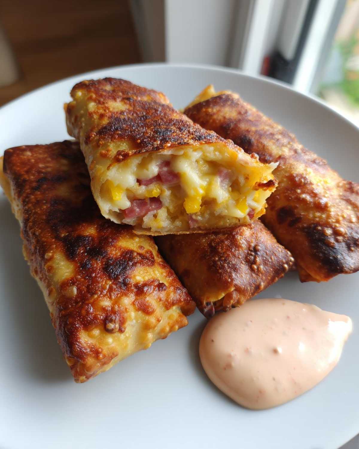 Close-up of crispy baked Reuben egg rolls piled on a plate next to a dollop of Thousand Island Dip.