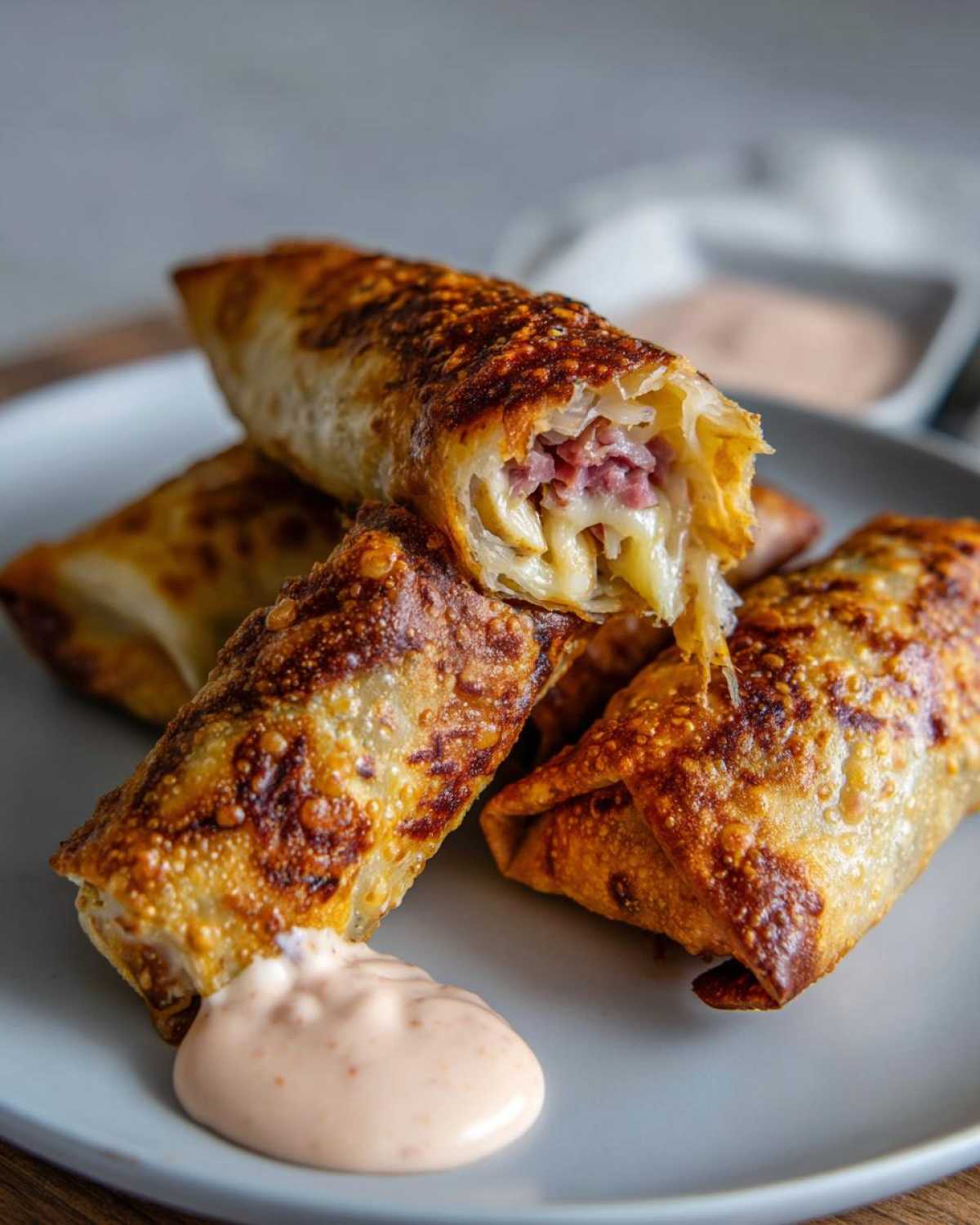 Close-up of crispy baked Reuben egg rolls, one cut open showing corned beef and melted cheese, served with Thousand Island Dip.