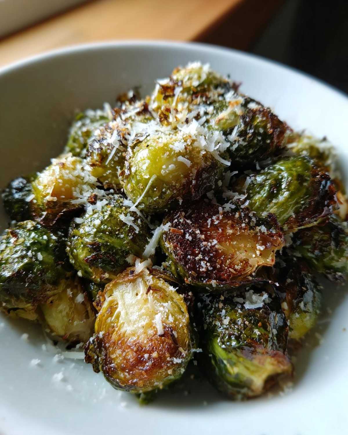 Close-up of roasted Crispy Parmesan Brussels Sprouts topped with grated cheese in a white bowl.