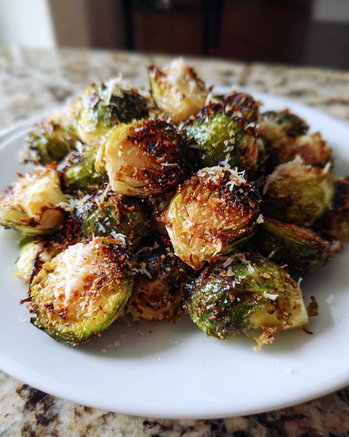A close-up of roasted and browned Crispy Parmesan Brussels Sprouts sprinkled with grated cheese on a white plate.