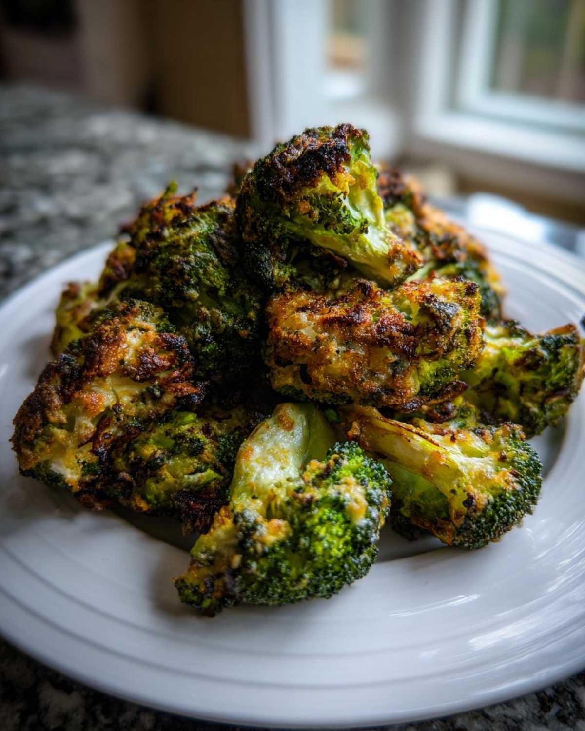 A pile of intensely roasted, Crispy Parmesan Roasted Broccoli florets on a white plate.