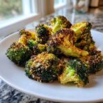 A close-up of perfectly roasted Crispy Parmesan Roasted Broccoli florets piled high on a white plate.