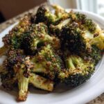 Close-up of deeply roasted, dark green Crispy Parmesan Roasted Broccoli florets piled on a white plate.