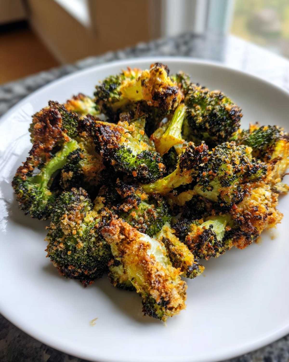 A pile of intensely roasted, crispy Parmesan roasted broccoli florets served on a white plate.