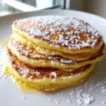 A close-up of a stack of four Fluffy Lemon Ricotta Pancakes dusted heavily with powdered sugar.