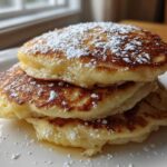 A tall stack of three Fluffy Lemon Ricotta Pancakes dusted heavily with powdered sugar on a white plate.