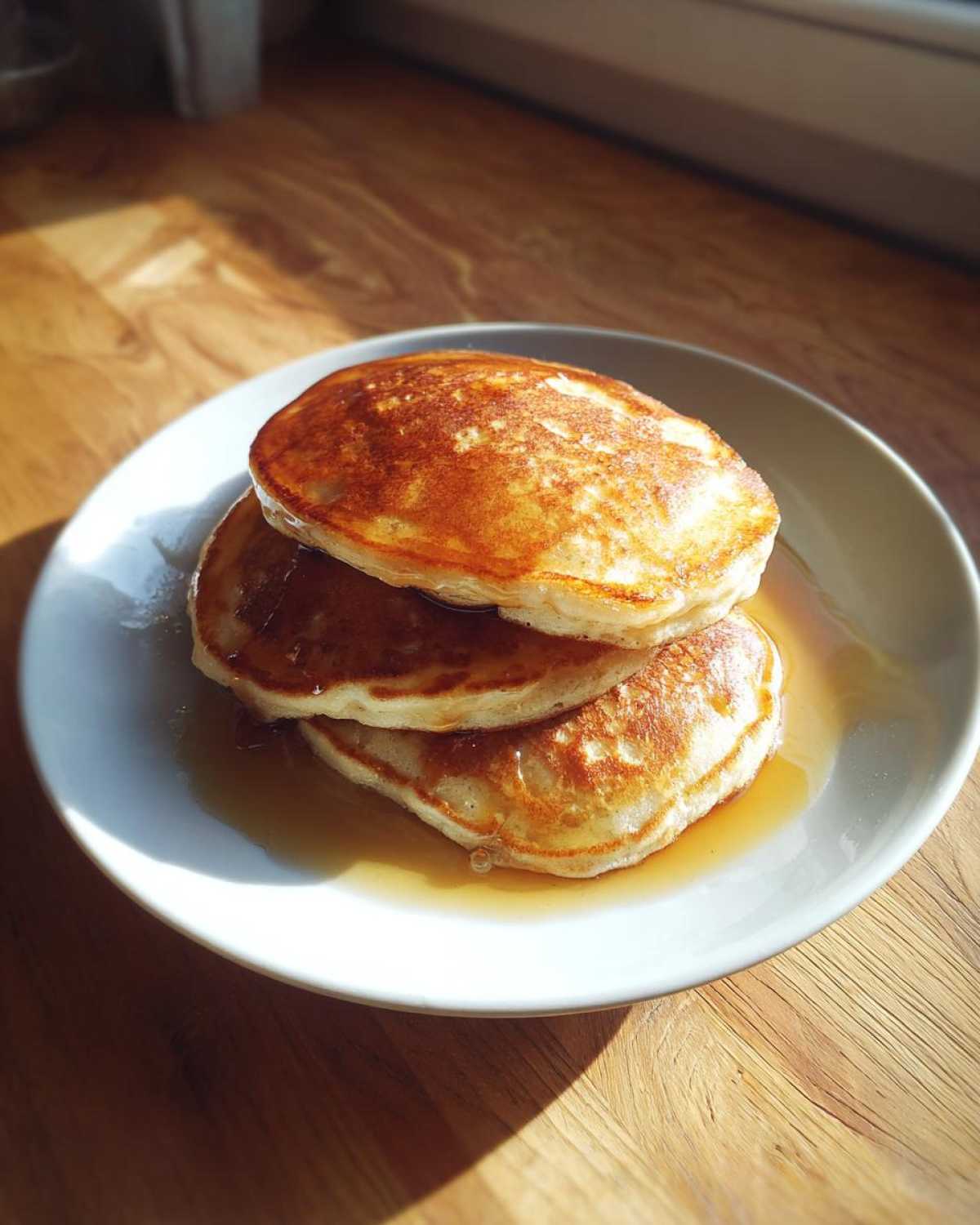 A stack of three fluffy Vegan Banana Oat Pancakes drizzled with syrup on a white plate.