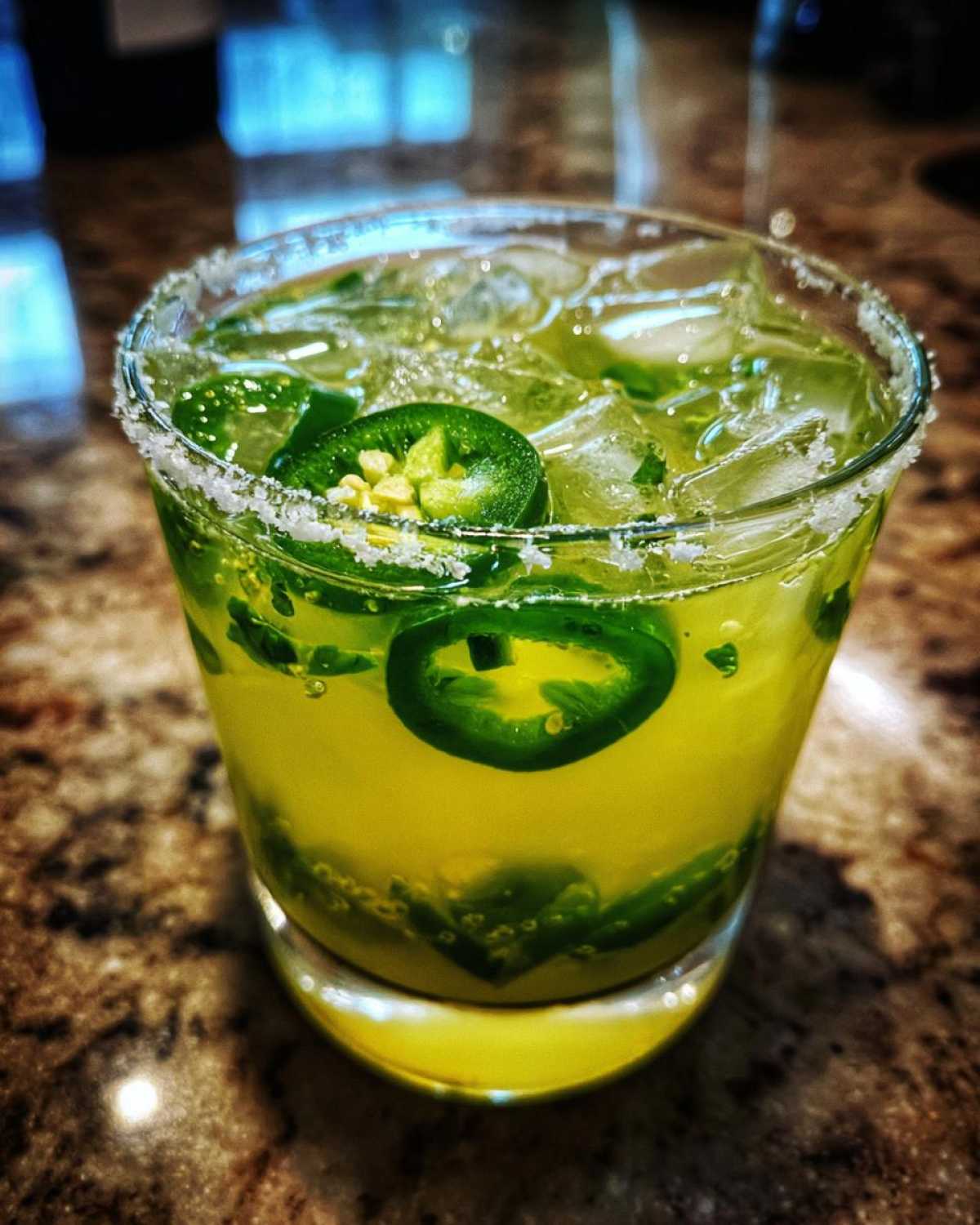 Close-up of a bright yellow Fresh Jalapeño Lime Margarita with ice and sliced jalapeños, served in a salt-rimmed glass.
