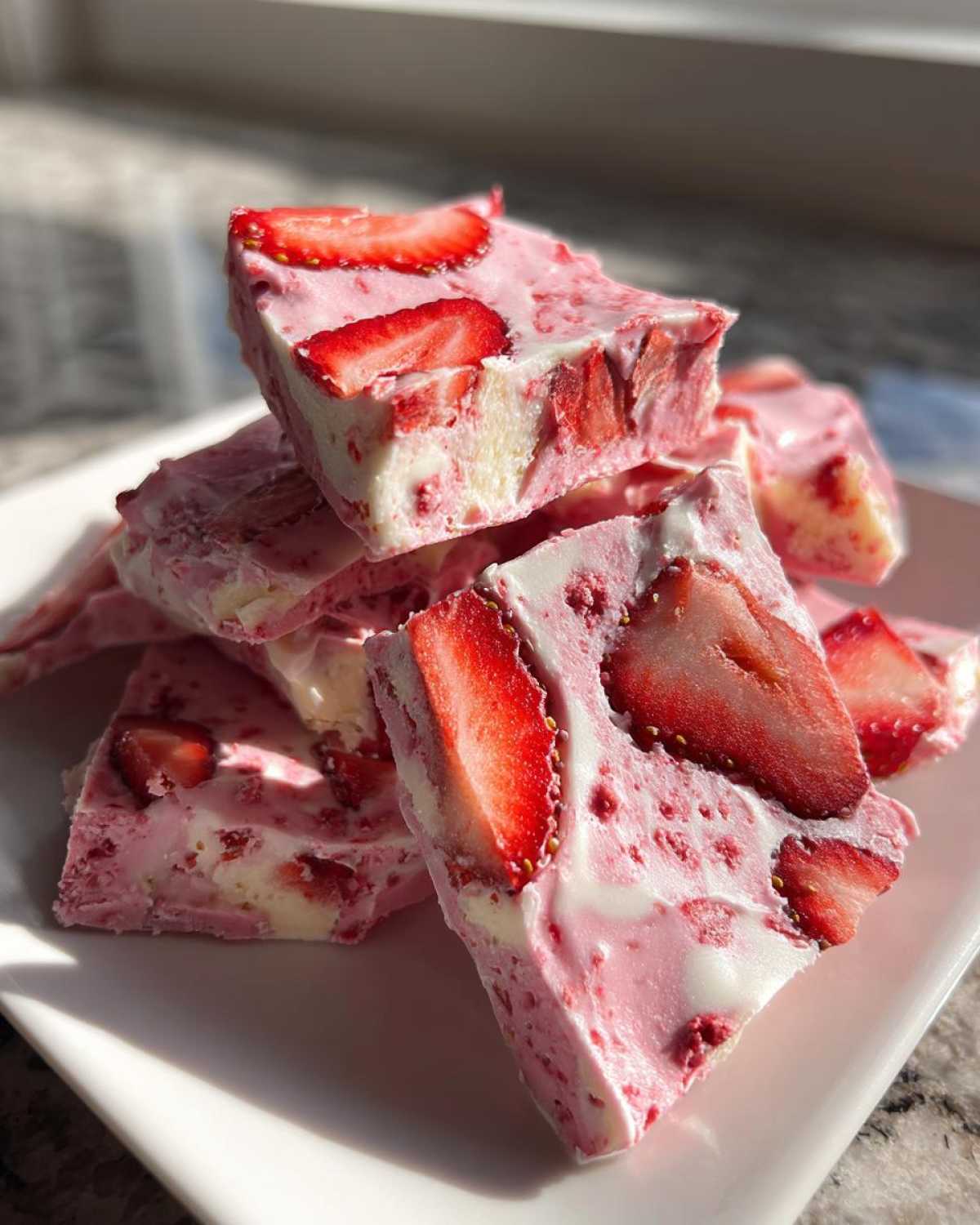 Close-up of stacked, pink and white pieces of Frozen Strawberry Yogurt Bark studded with fresh strawberry slices.