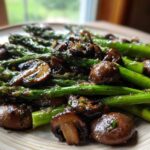 A plate of vibrant green asparagus spears mixed with glossy brown roasted mushrooms, coated in garlic butter.
