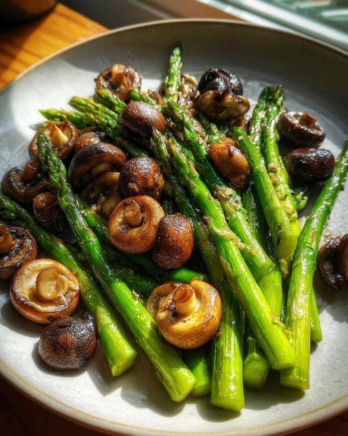 Bright green roasted asparagus spears mixed with browned mushrooms, coated in garlic butter.