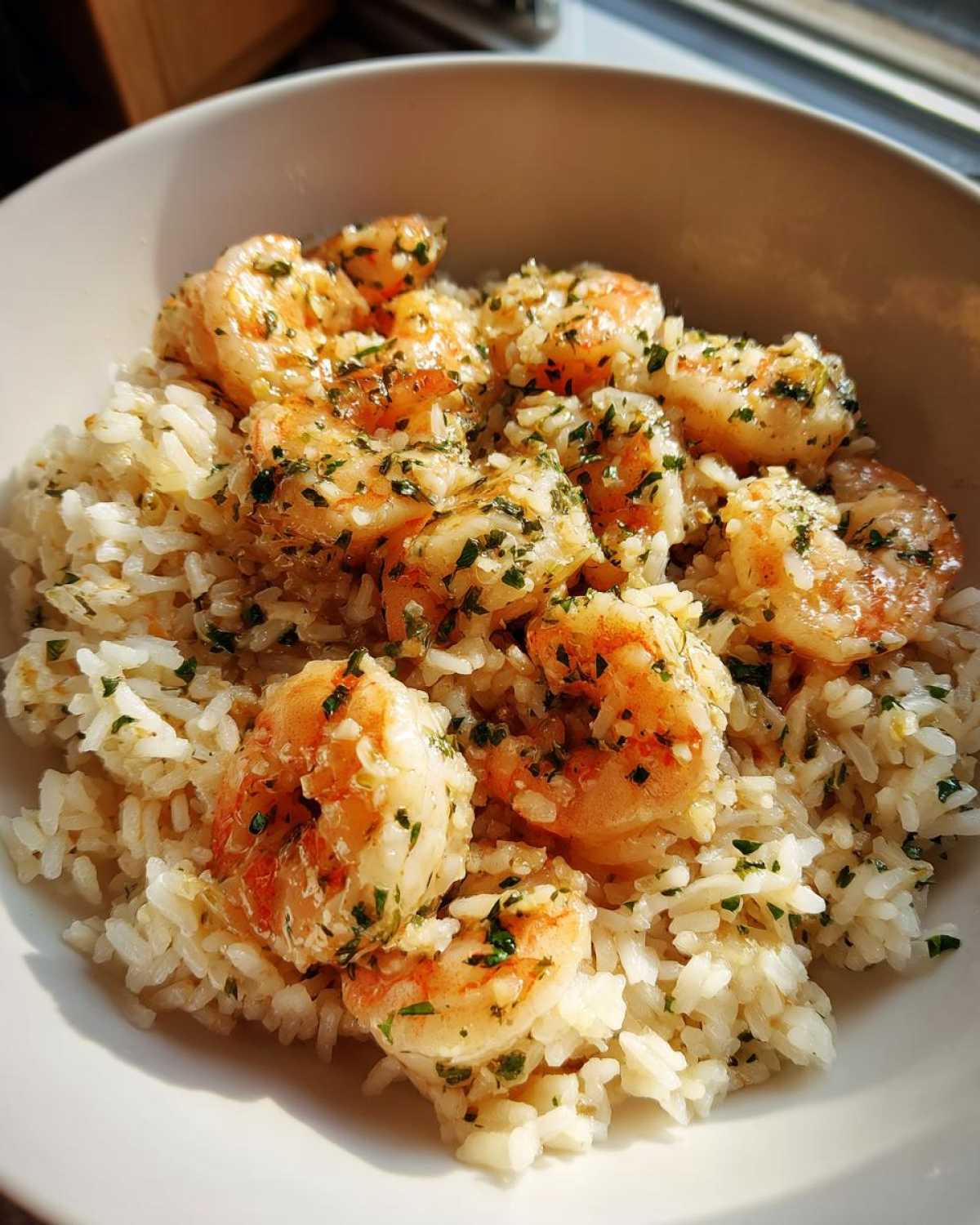 Close-up of Garlic Butter Shrimp and Rice Skillet served in a white bowl, glistening with butter sauce and parsley.