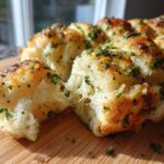 A piece of golden-brown Garlic Parmesan Pull-Apart Bread is being pulled apart, showing melted cheese stretching between the soft interior.