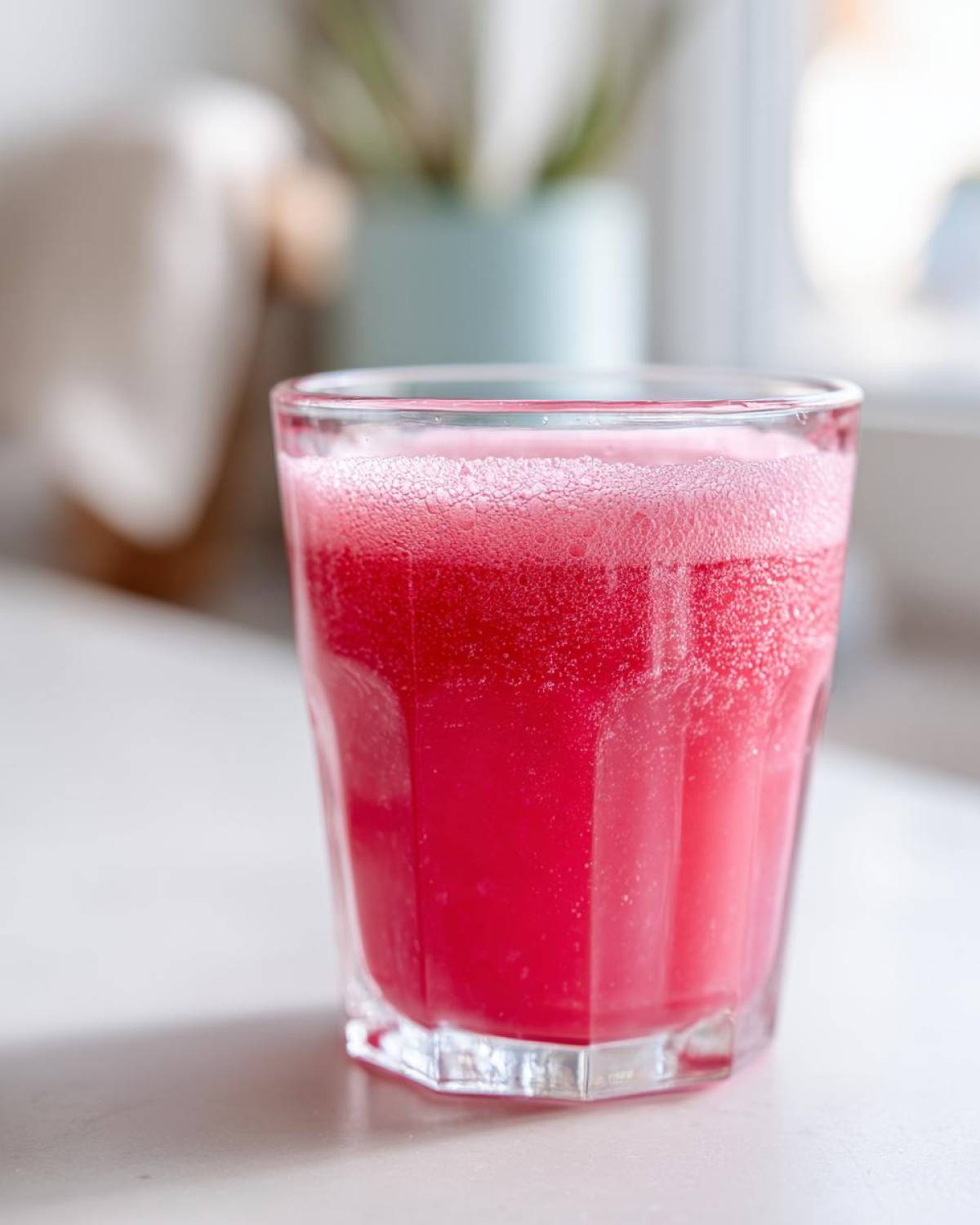 A close-up of a vibrant pink drink, likely prepared from Homemade Strawberry Lemonade Concentrate, with foam on top.