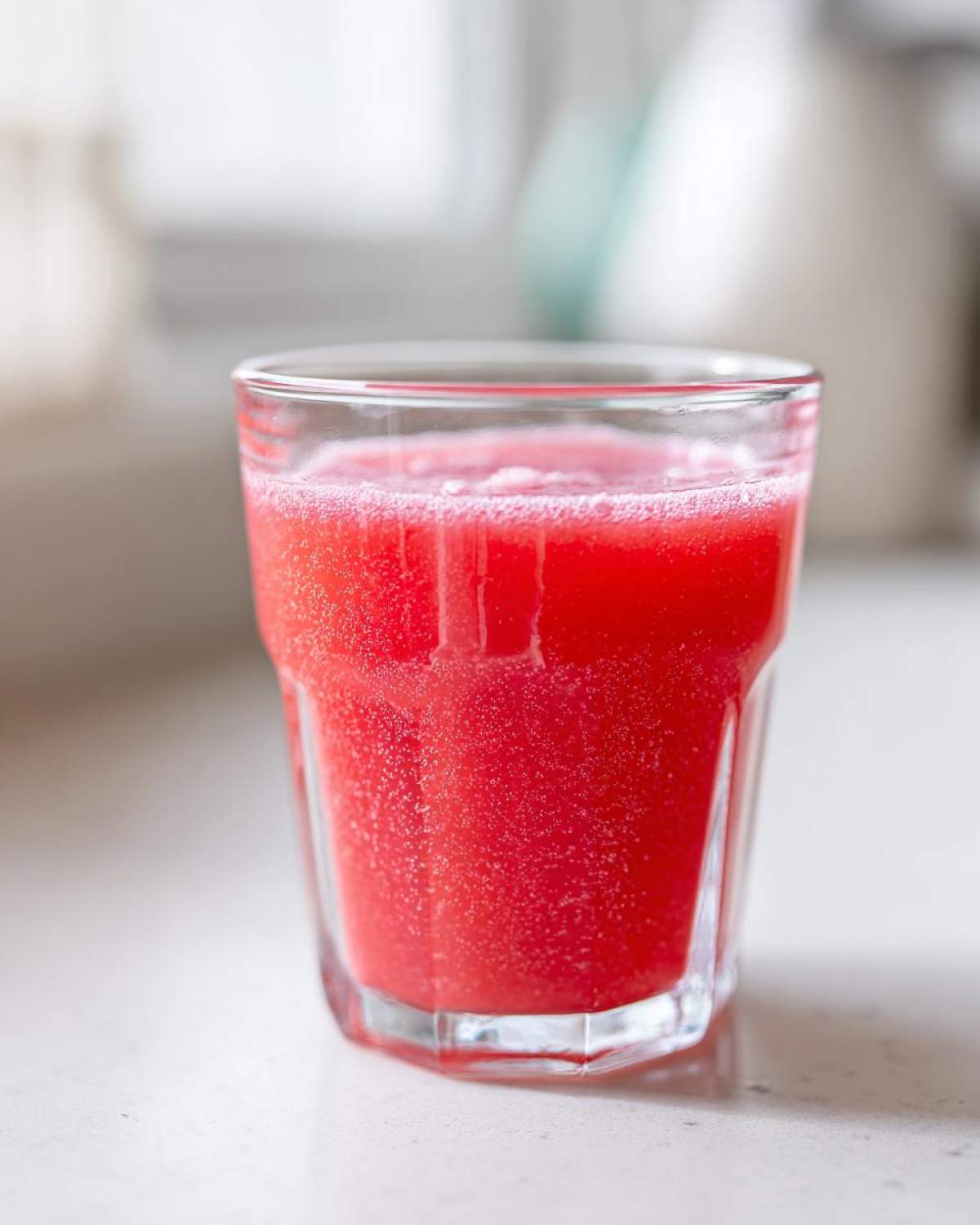 Close-up of a glass filled with vibrant red liquid, likely the Homemade Strawberry Lemonade Concentrate mixed with water.
