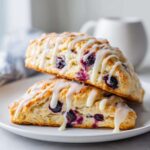 Two stacked Blueberry Lemon Scones drizzled generously with white lemon glaze, showing baked blueberries inside.