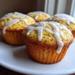 Four freshly baked Glazed Lemon Poppy Seed Muffins topped with a thick, white lemon drizzle.