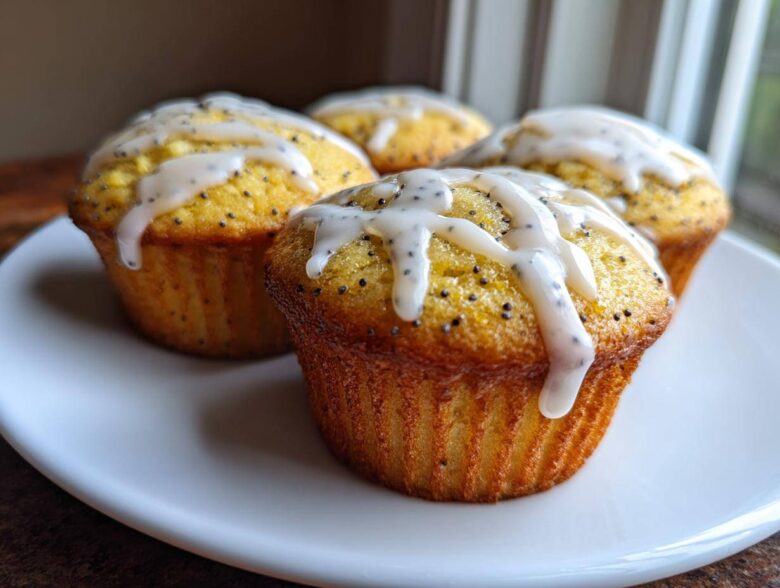 Four freshly baked Glazed Lemon Poppy Seed Muffins topped with a thick, white lemon drizzle.