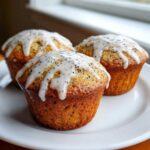 Three golden-brown Glazed Lemon Poppy Seed Muffins topped with thick, dripping lemon glaze and visible poppy seeds.