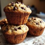 A close-up stack of three freshly baked Gluten-Free Banana Chocolate Chip Muffins topped with melted chocolate chips.