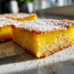 A close-up, bright photo of a square slice of bright yellow Gluten-Free Lemon Bars topped with powdered sugar.