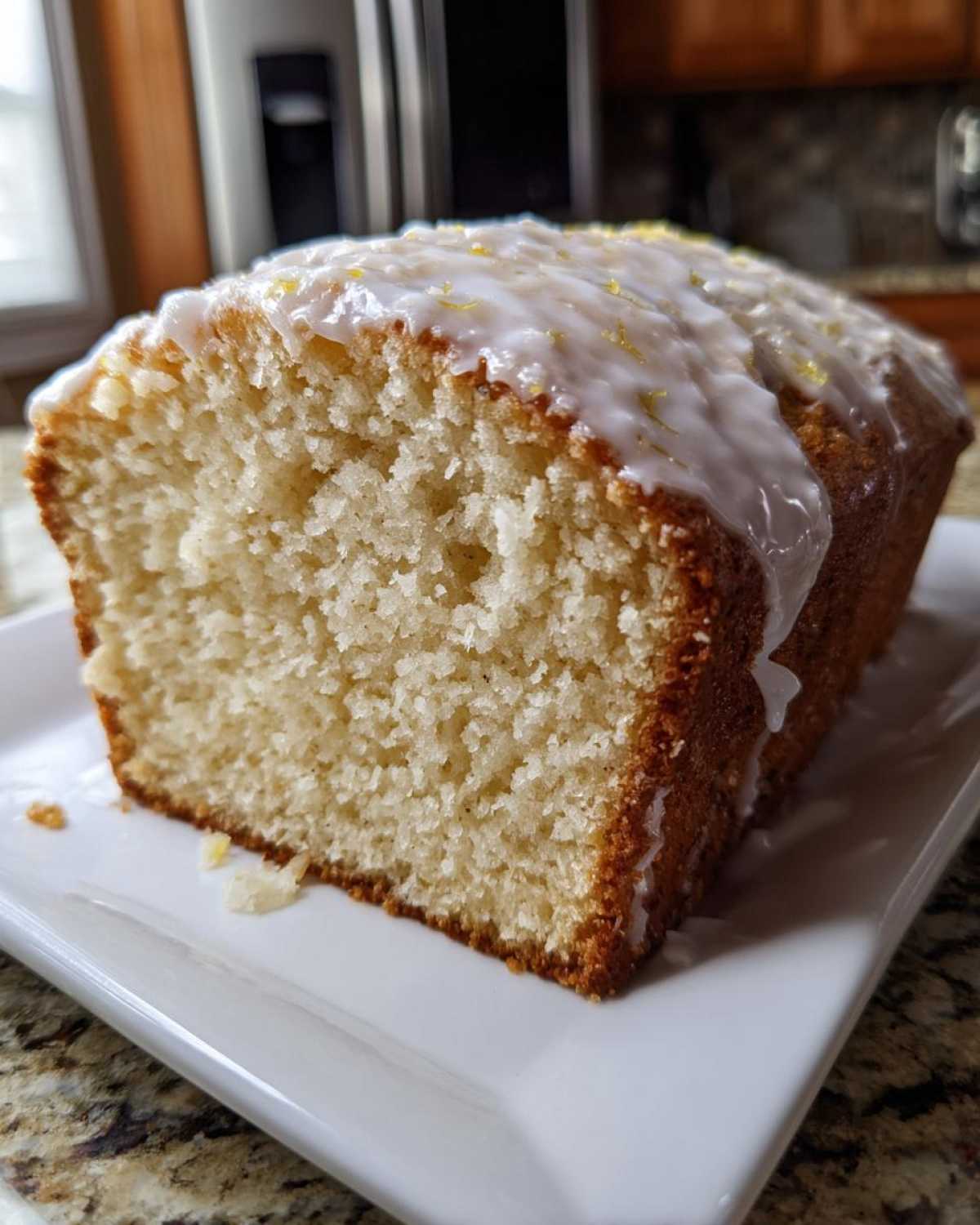 Close-up of a slice of moist Gluten-Free Lemon Coconut Cake loaf with white glaze and lemon zest.