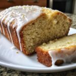 Close-up of a moist Gluten-Free Lemon Coconut Cake loaf, drizzled with white lemon icing and zest.