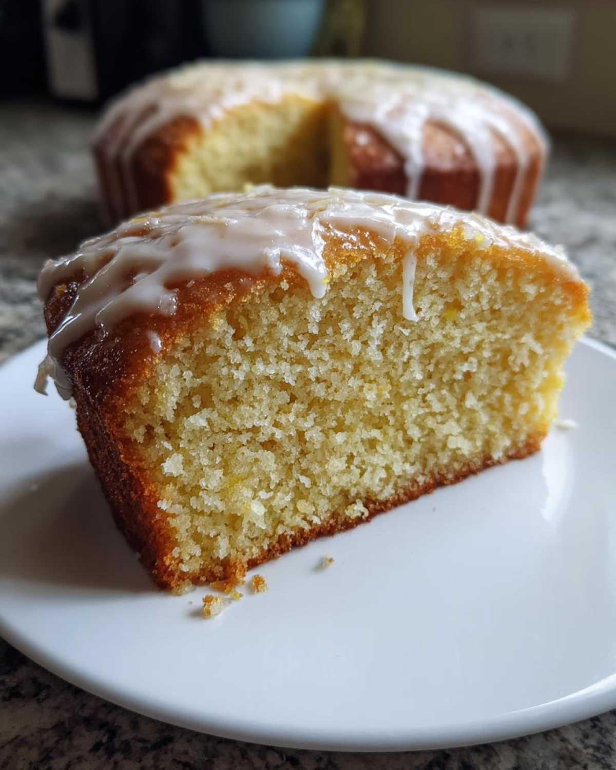 A close-up slice of moist Gluten-Free Lemon Coconut Cake topped with a white lemon glaze.