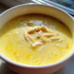 A close-up of rich, yellow Greek Lemon Chicken Soup with shredded chicken and orzo pasta.