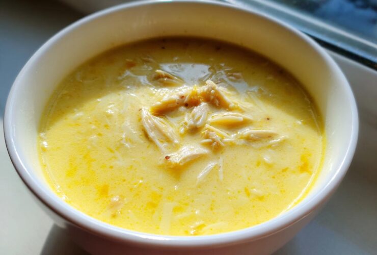A close-up of rich, yellow Greek Lemon Chicken Soup with shredded chicken and orzo pasta.