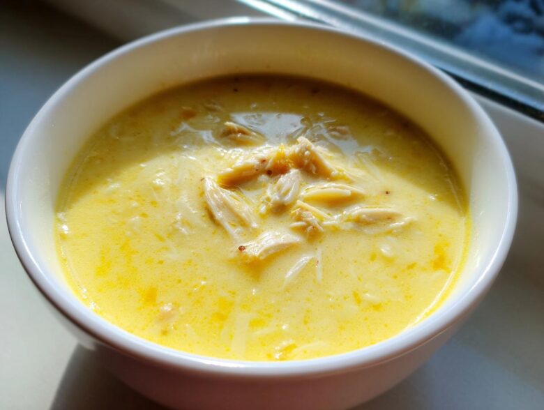 A close-up of rich, yellow Greek Lemon Chicken Soup with shredded chicken and orzo pasta.