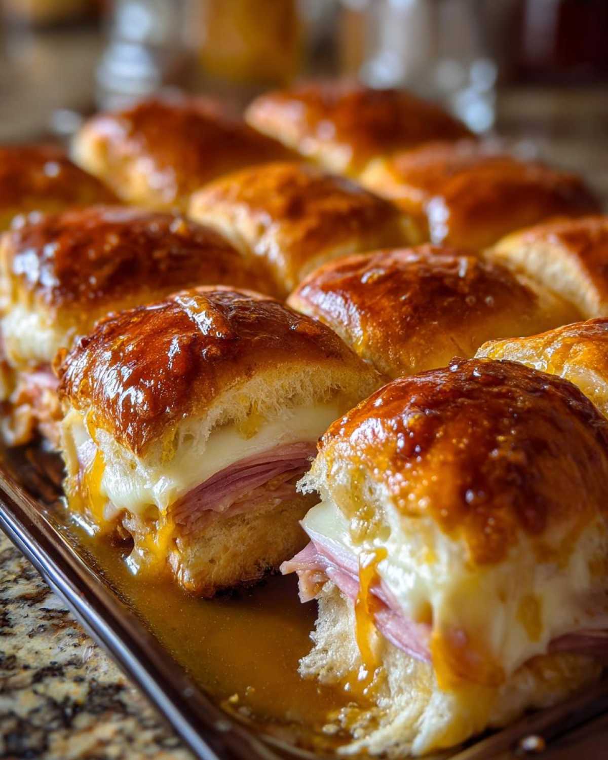 Close-up of baked Hawaiian Roll Ham and Cheese Sliders covered in a shiny honey mustard glaze, with melted cheese oozing out.