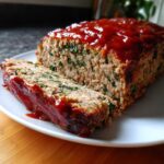 A slice cut from a Healthy Turkey Spinach Meatloaf, topped with a thick, shiny red glaze.
