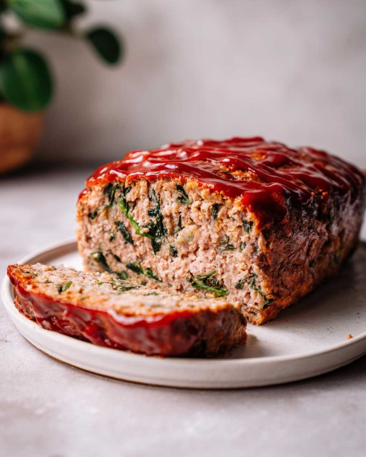 A sliced Healthy Turkey Spinach Meatloaf topped with a thick, glossy ketchup glaze on a white plate.
