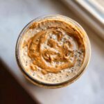 Overhead view of creamy High-Protein Peanut Butter Overnight Oats topped with a swirl of peanut butter and chia seeds in a glass jar.