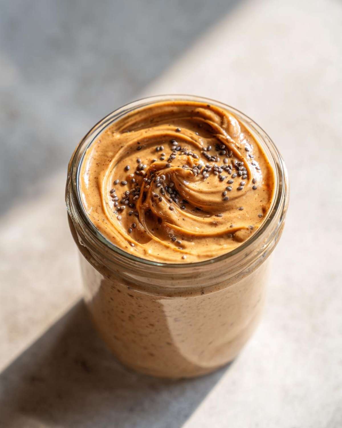 Overhead close-up of creamy High-Protein Peanut Butter Overnight Oats topped with chia seeds in a glass jar.