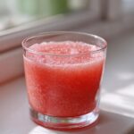 Close-up of a glass filled with a bright pink, icy beverage made from Homemade Strawberry Lemonade Concentrate.