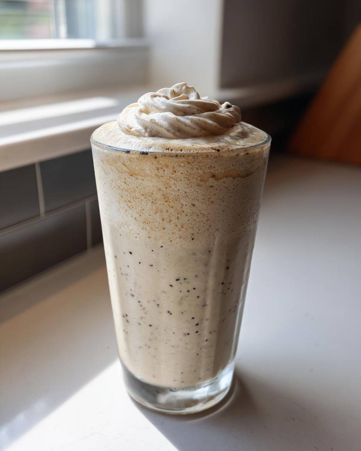 A tall glass of Homemade Vanilla Bean Frappuccino topped with whipped cream, showing vanilla bean specks.
