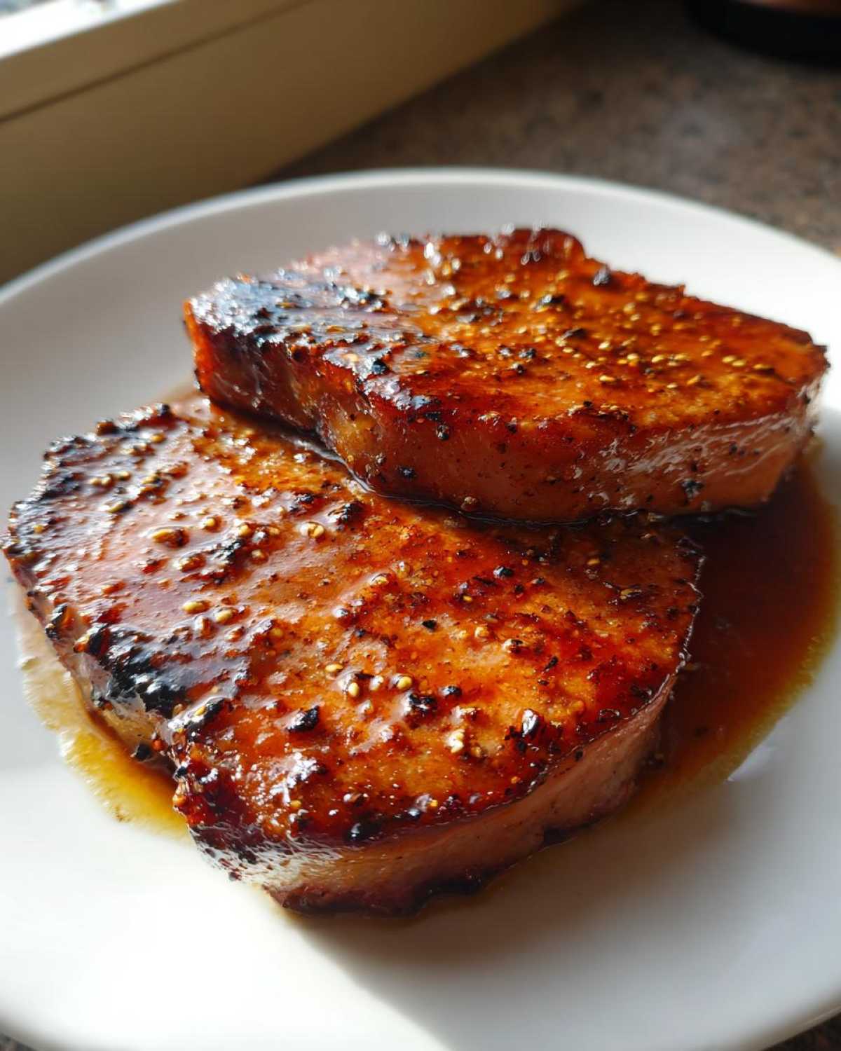 Close-up of two thick Honey Glazed Ham Steak in the Skillet portions served on a white plate with extra glaze.