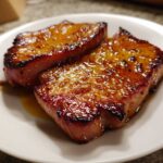 Close-up of two perfectly caramelized Honey Glazed Ham Steak in the Skillet served on a white plate.