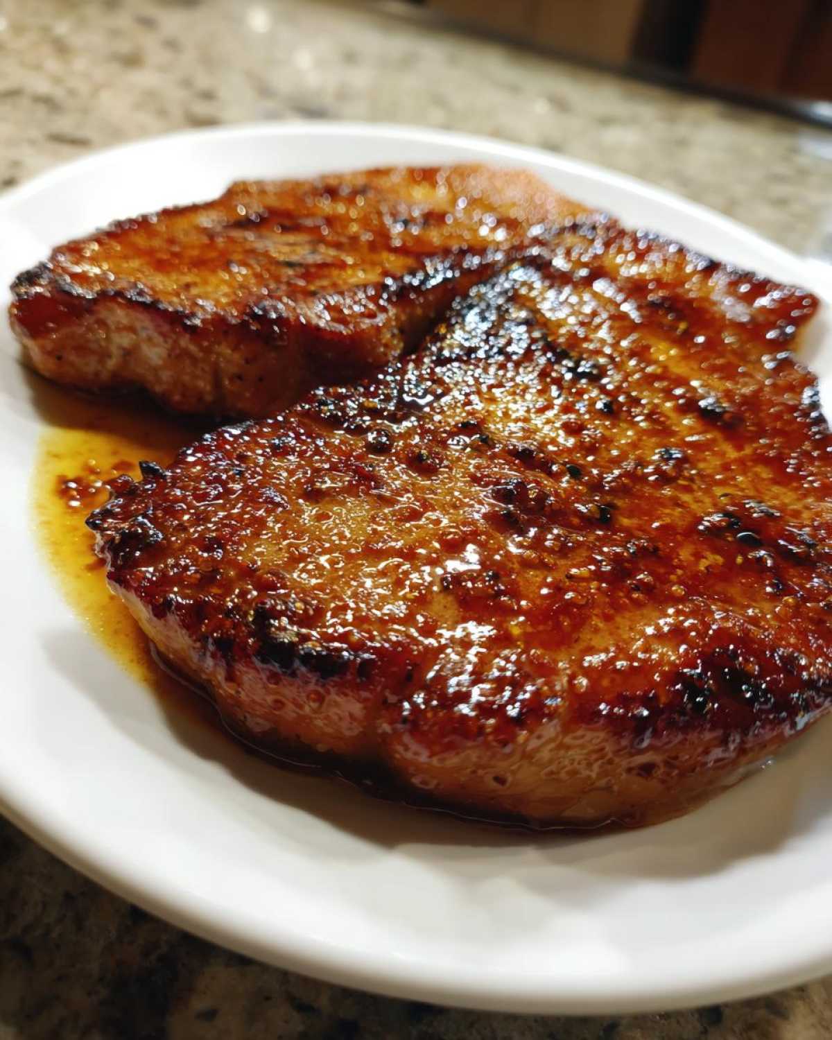 Close-up of two perfectly seared Honey Glazed Ham Steak in the Skillet, glistening with sweet glaze on a white plate.