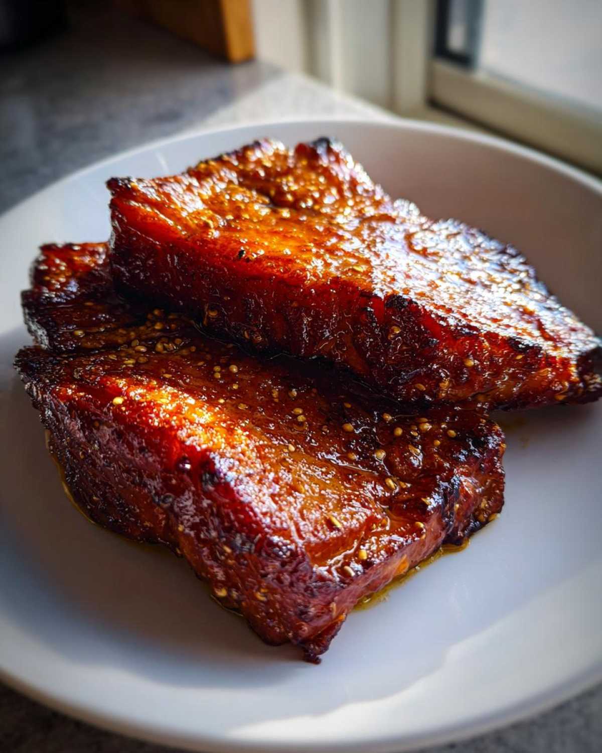 Close-up of two thick Honey Glazed Ham Steak in the Skillet pieces on a white plate, glistening with glaze.