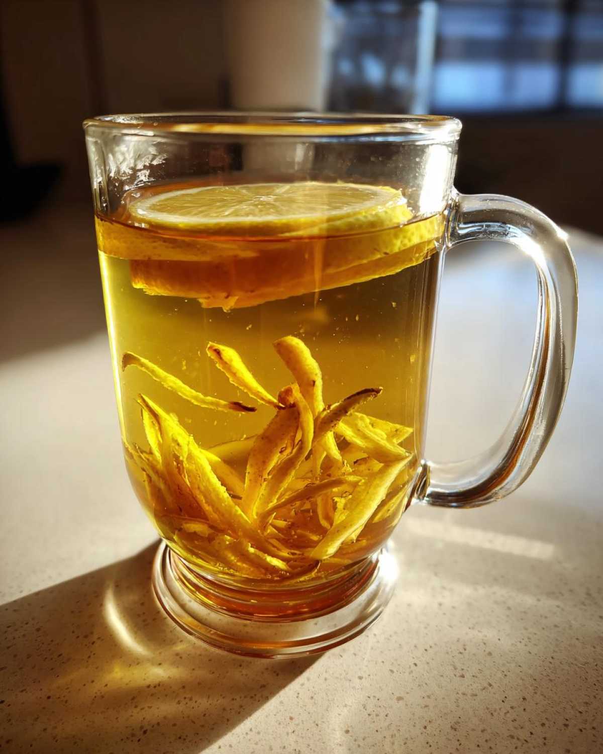 Close-up of Honey Lemon Ginger Tea steeping in a clear glass mug with ginger strips and lemon slices.