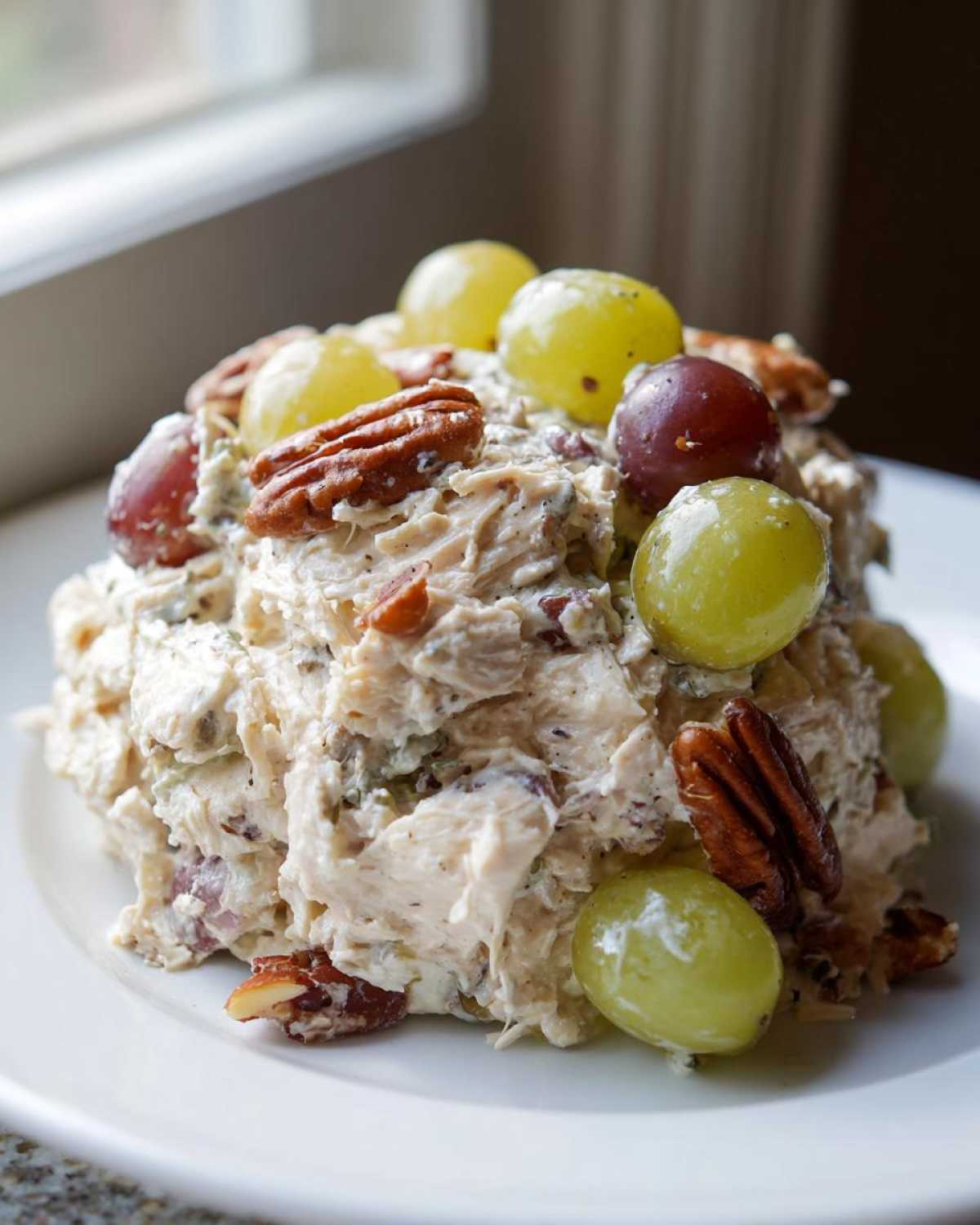 A scoop of creamy Honey Mustard Chicken Salad with Grapes, topped with pecans and whole grapes, served on a white plate.