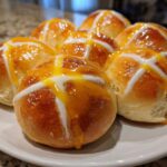 A plate of freshly baked Hot Cross Buns with Orange Glaze, featuring a shiny glaze and white icing crosses.