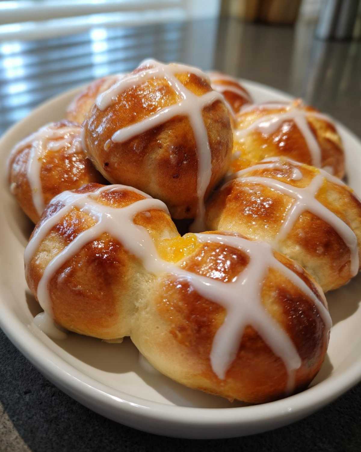 A close-up of several golden brown Hot Cross Buns with Orange Glaze topped with thick white icing crosses.