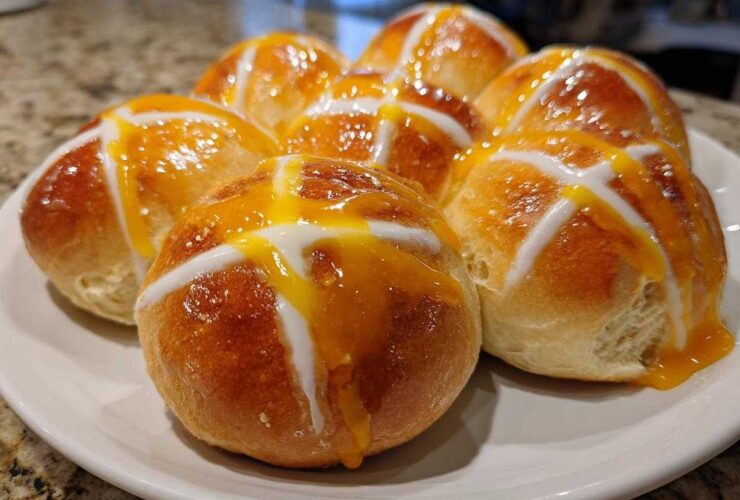 A plate of freshly baked Hot Cross Buns with Orange Glaze, featuring a shiny glaze and white icing crosses.